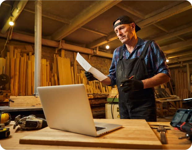 A tradesperson in a workshop using a laptop.