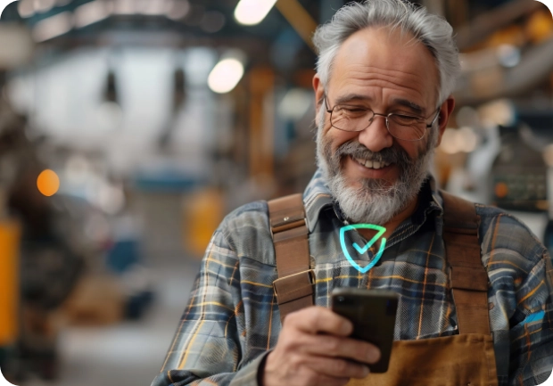 Smiling older craftsman in overalls using a smartphone in a workshop.